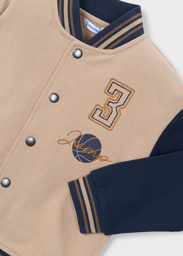 Деталі бежевого varsity бомбера для хлопчика в спортивному стилі: контрастні рукави, кнопки та смугасті манжети